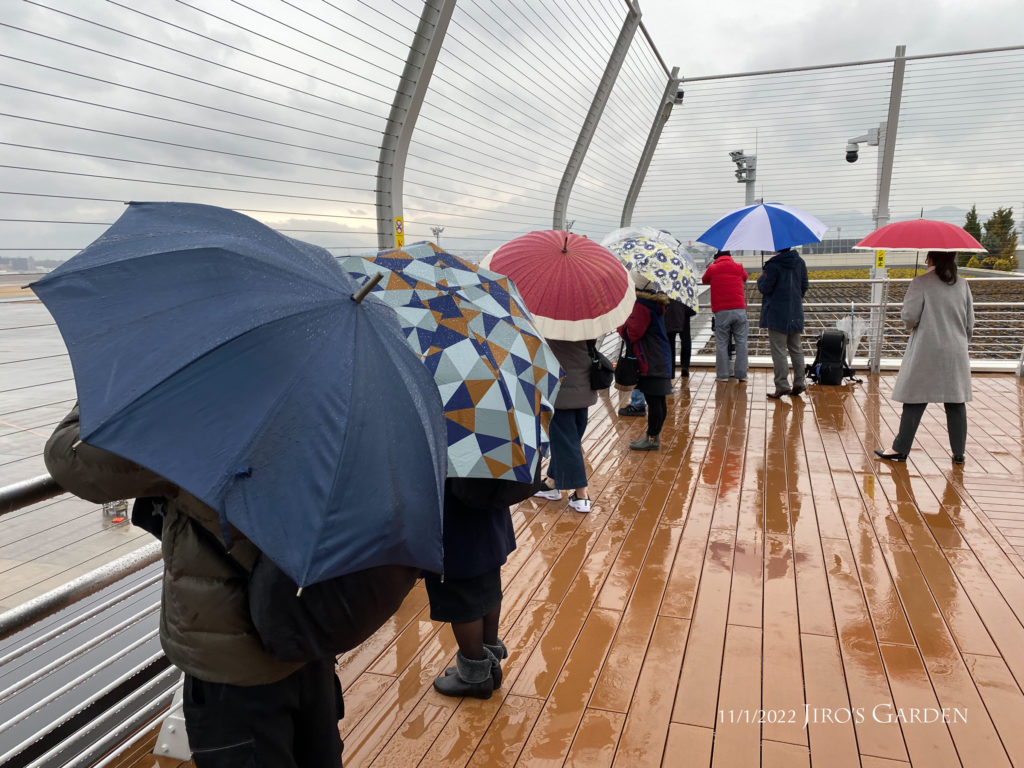 北ターミナルの展望デッキで傘を差して見守る人々。