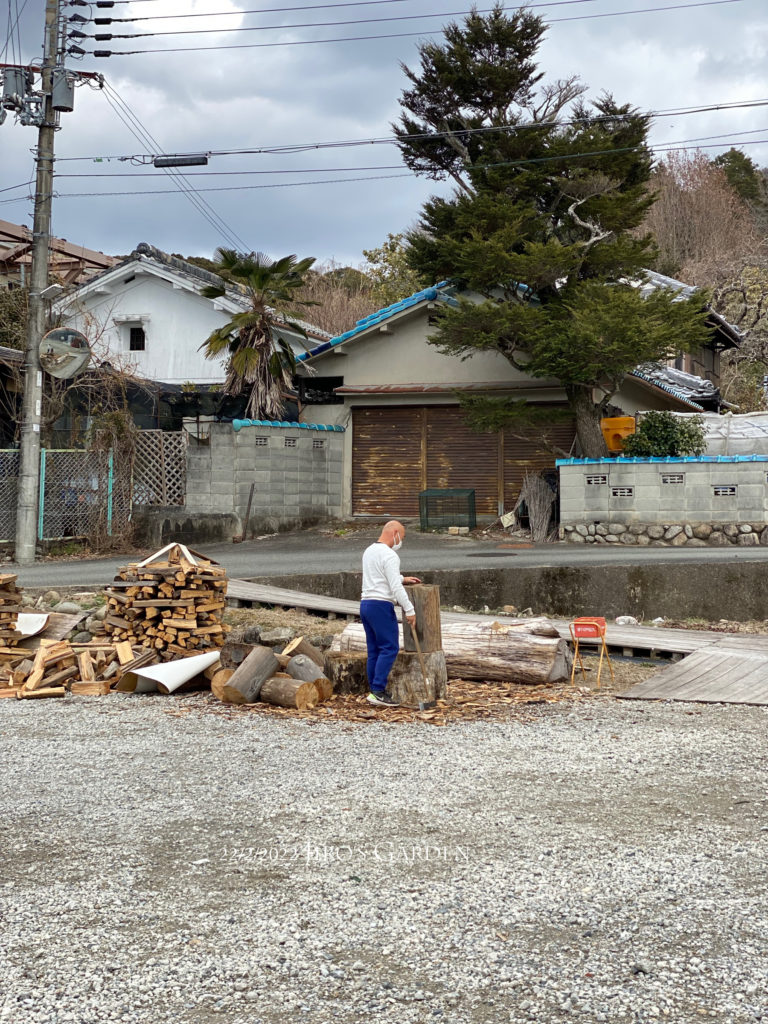 小屋の外、駐車場の端っこで薪割りをするおじさん。
