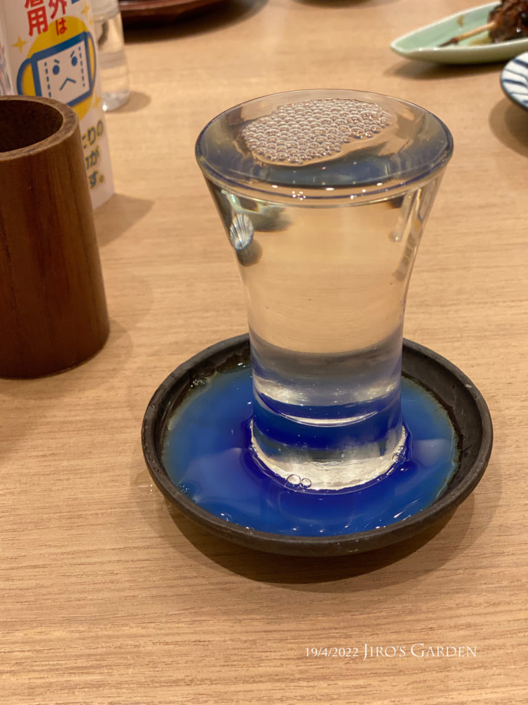 ガラスのグラスにあふれる日本酒。丸い受け皿は湖のような深い青色。